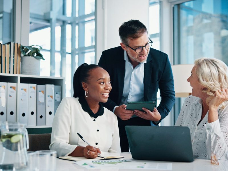 Accounting, office and business people with meeting, feedback and manager for laptop, discussion and graphs. Training, teamwork and talk with tablet, growth strategy or project report for finance Team of 3 in at an office table, smiling in collaboration