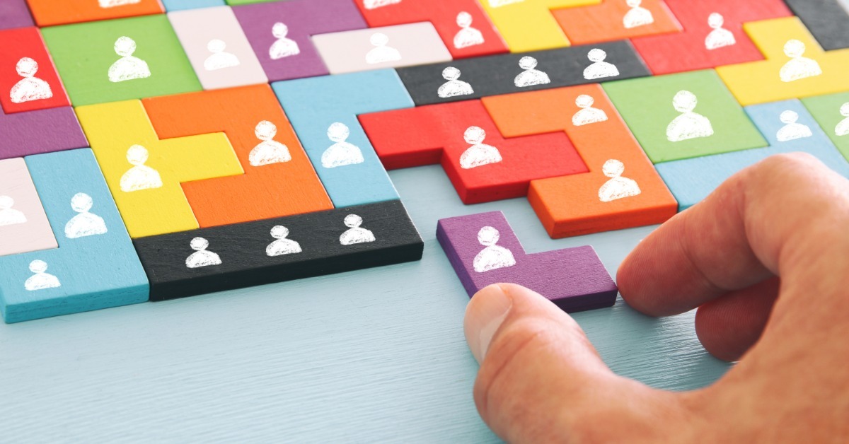 A hand places a purple puzzle piece into a colorful Tetris-style layout of connected blocks marked with white person icons.