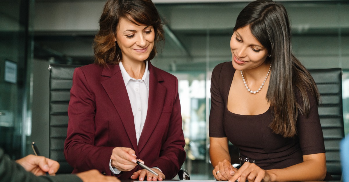 Two professionals sitting at a table looking at a document. Another employee sits across the table from them.