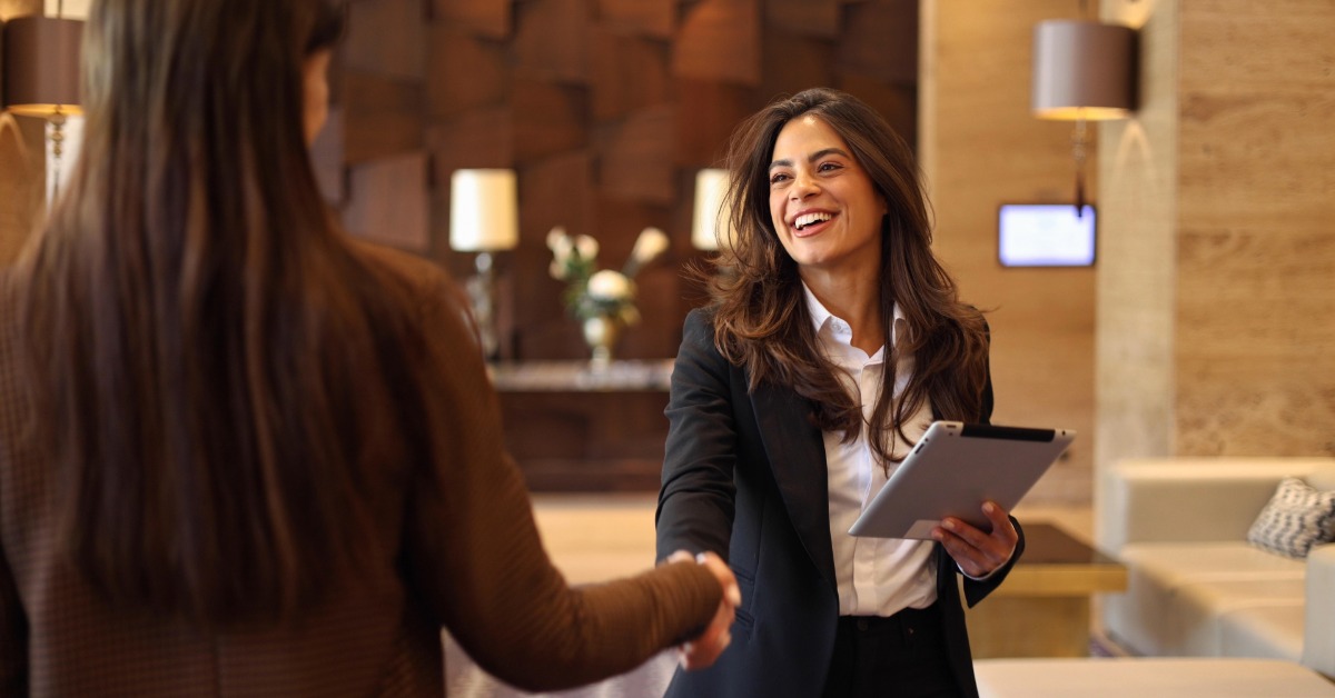 A professional wearing a business suit and holding a tablet shakes hands with an employee in a lobby.
