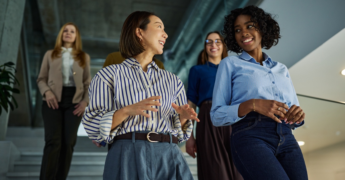 Five professionally dressed employees walking down a large staircase in a brightly lit office space.
